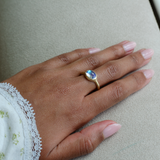 Model Hand wearing a solid 14k gold unisex signet ring with bezel set bright blue sheen moonstone. Gold ring has brushed, matte finish