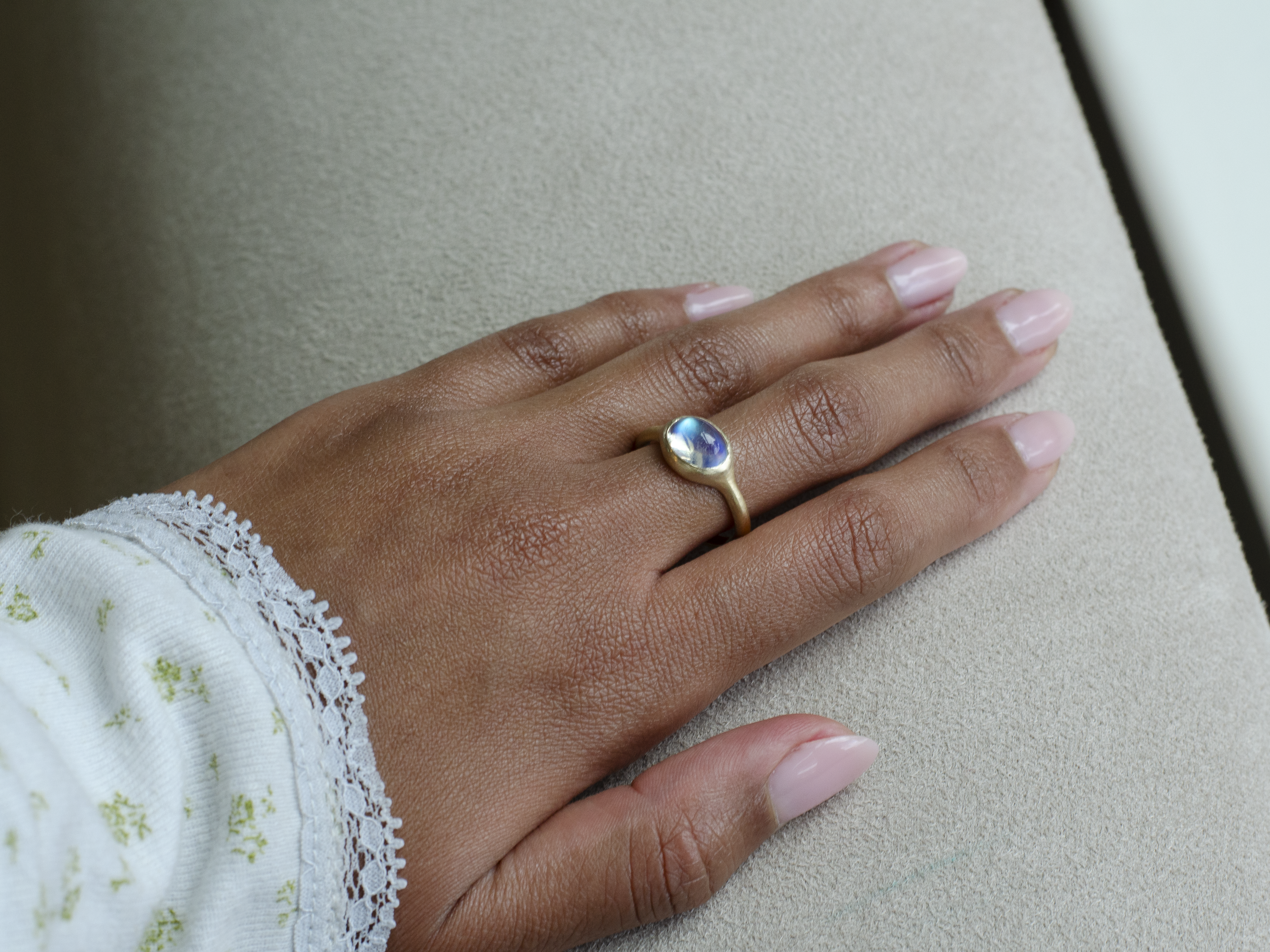 Model Hand wearing a solid 14k gold unisex signet ring with bezel set bright blue sheen moonstone. Gold ring has brushed, matte finish