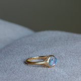 side view of solid 14k yellow gold signet ring with bezel set bright blue sheen moonstone. Gold ring has brushed, matte finish