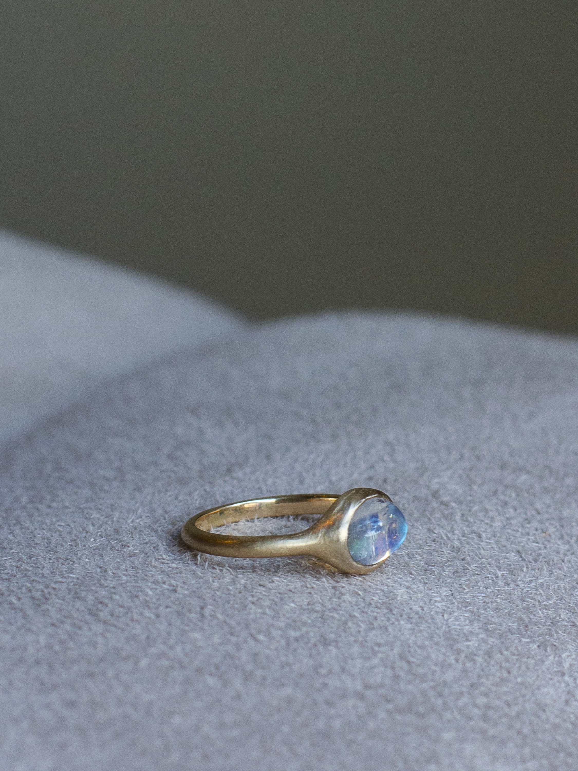 side view of solid 14k yellow gold signet ring with bezel set bright blue sheen moonstone. Gold ring has brushed, matte finish