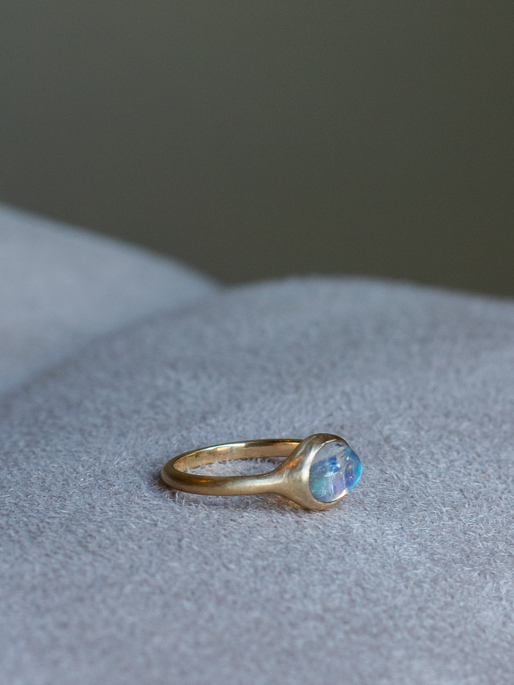 side view of solid 14k yellow gold signet ring with bezel set bright blue sheen moonstone. Gold ring has brushed, matte finish