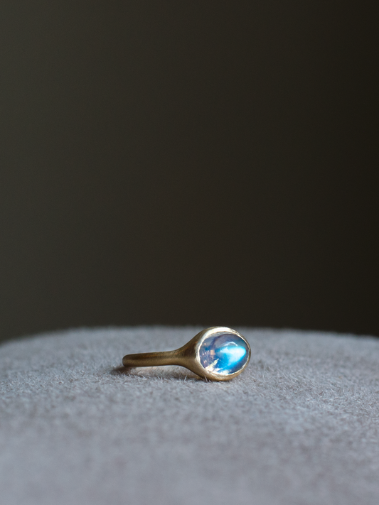 solid 14k yellow gold signet ring with bezel set bright blue sheen oval cabochon moonstone. Gold ring has brushed, matte finish