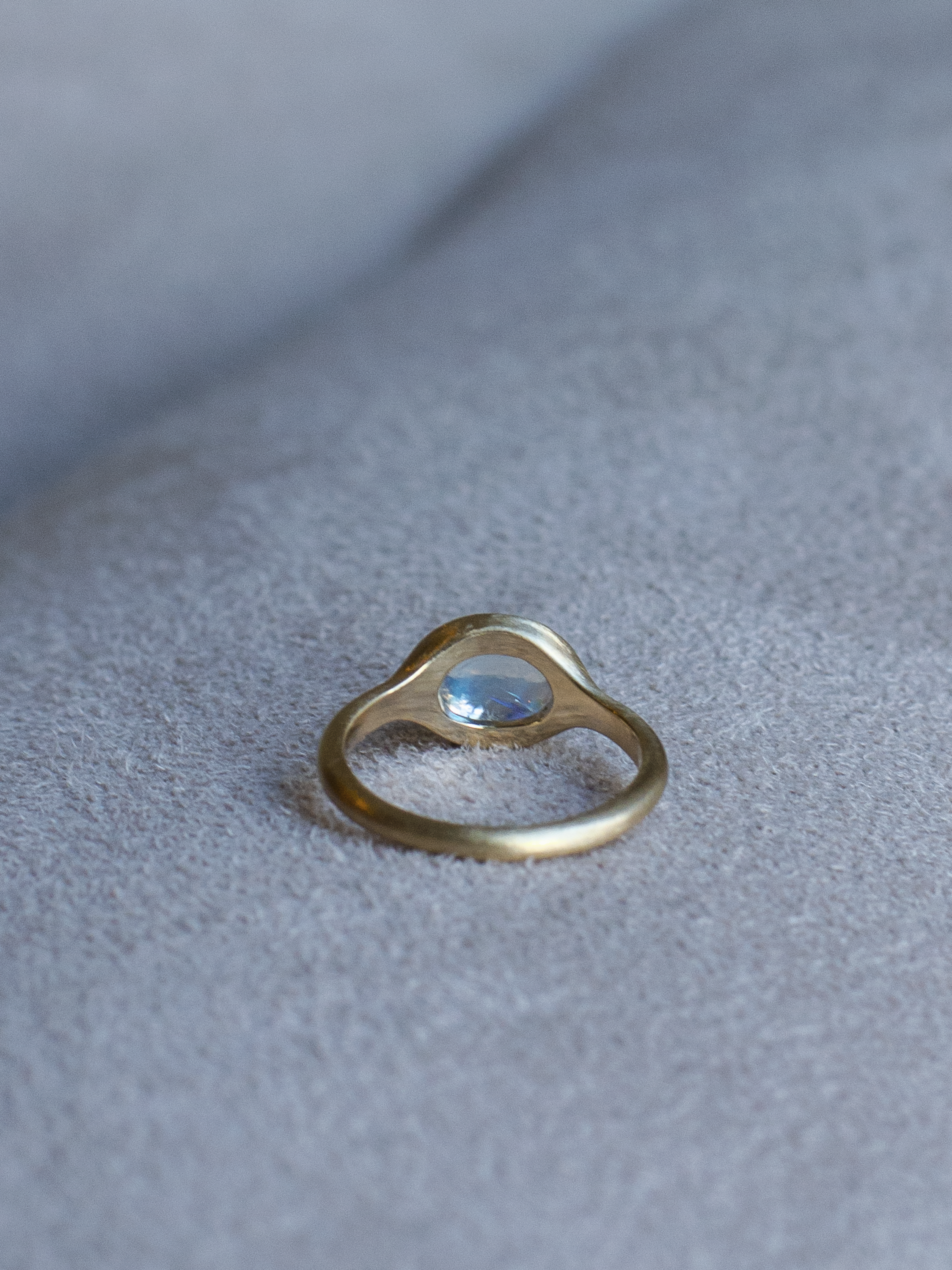 Back view of solid 14k yellow gold signet ring with bezel set bright blue sheen moonstone. Gold ring has brushed, matte finish
