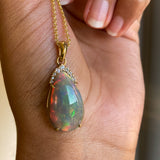 Natural Black Opal and diamond pear cut pendant on a gold chain held by a hand