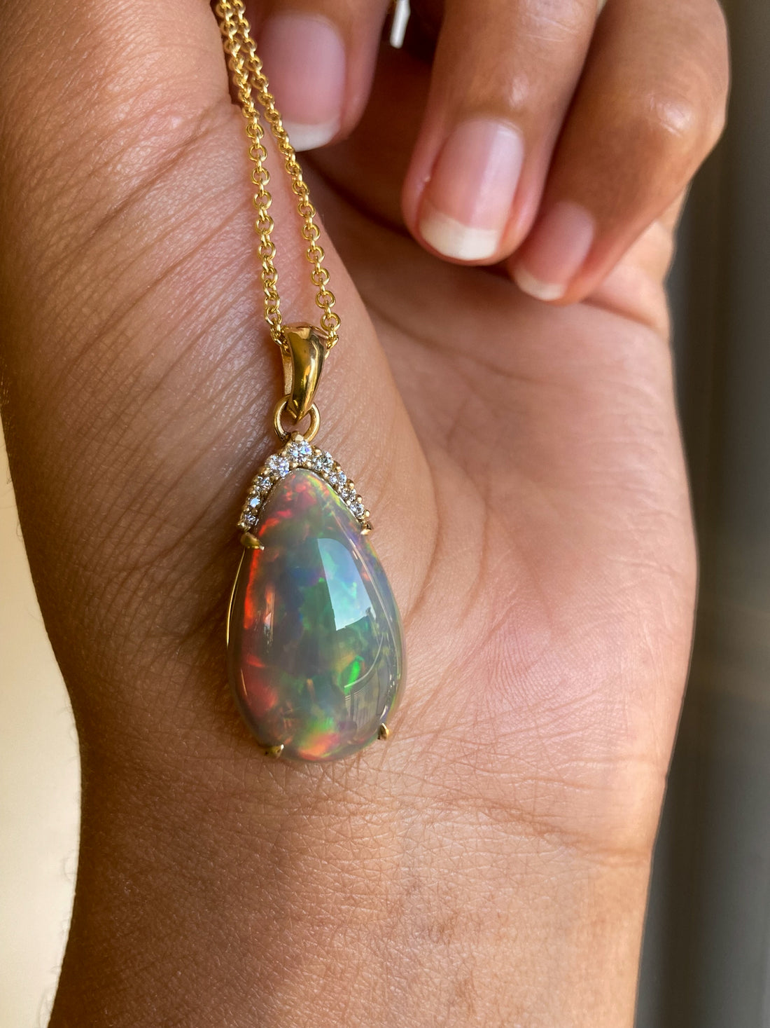 Natural Black Opal and diamond pear cut pendant on a gold chain held by a hand