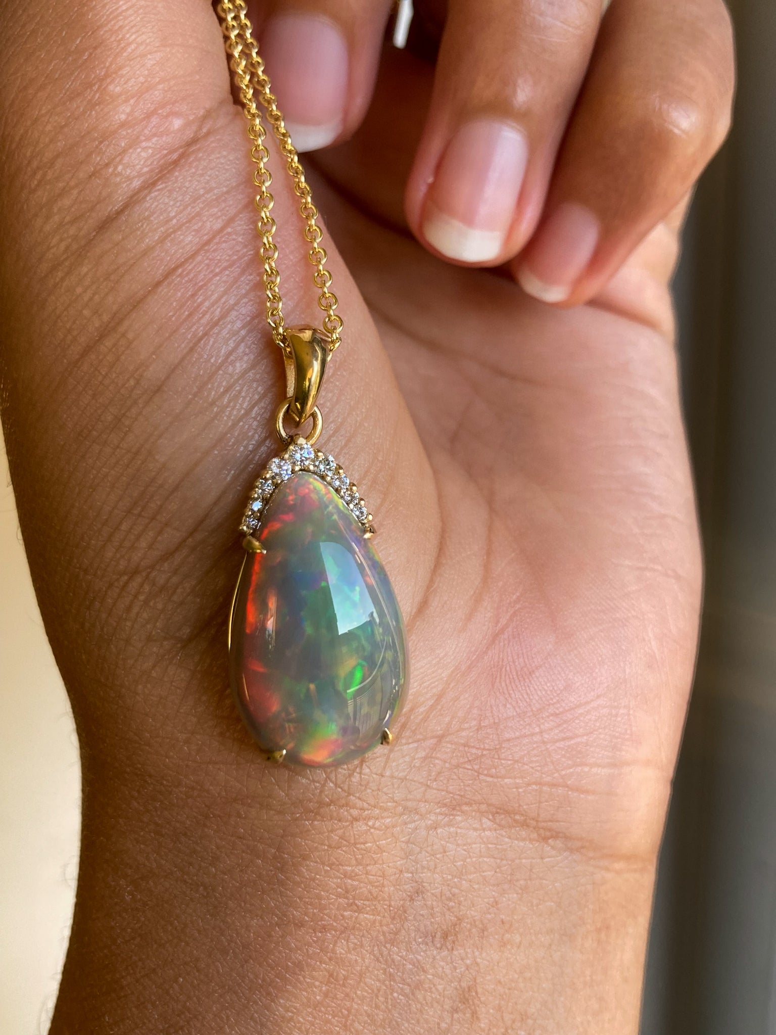 Natural Black Opal and diamond pear cut pendant on a gold chain held by a hand