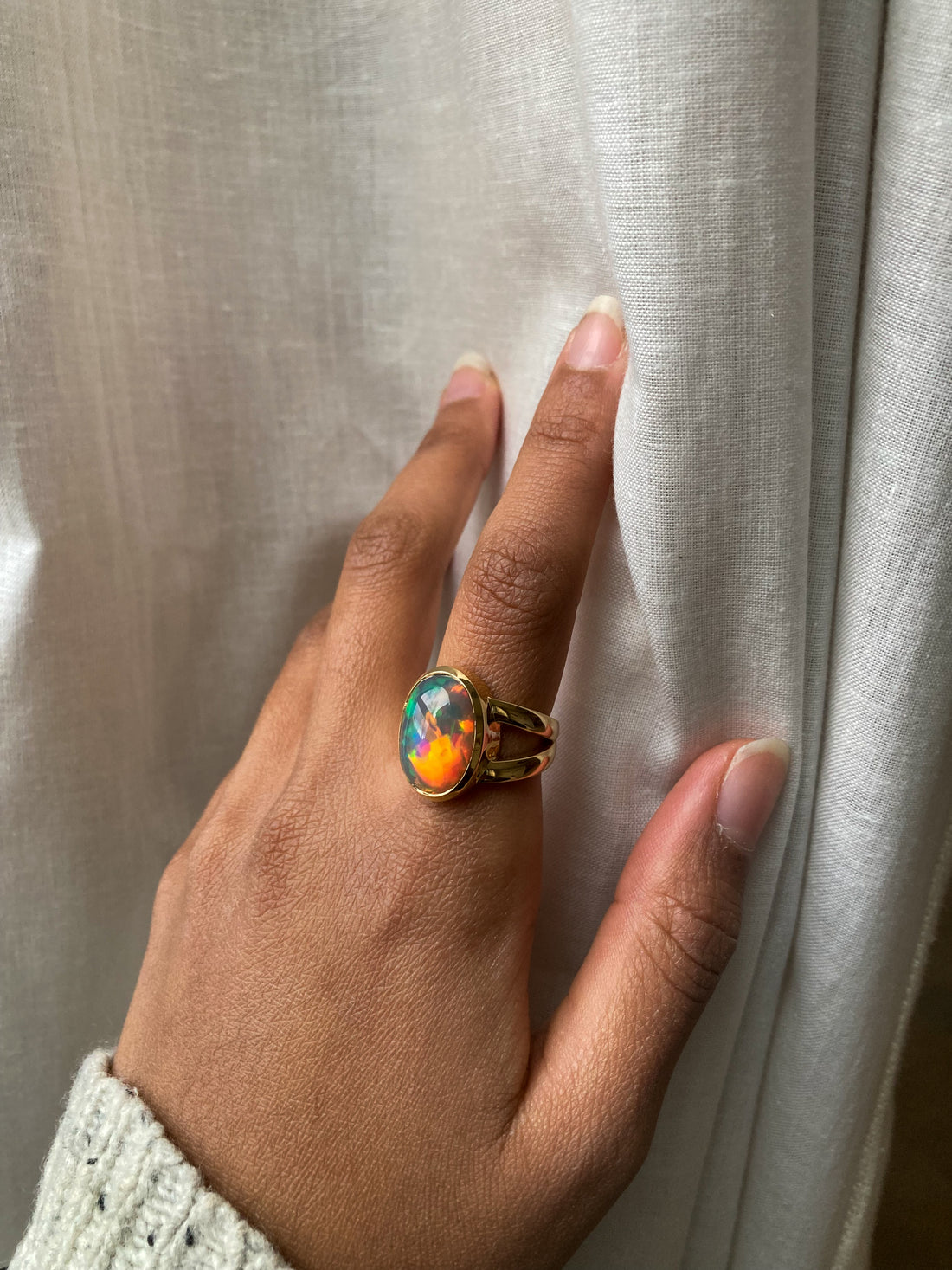 Large Black opal with rainbow and red fire bezel set in solid 14k yellow gold statement ring with split shank. Worn on model's hand