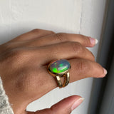 Large Oval cut Black opal with green fire bezel set in solid 14k yellow gold statement ring with split shank. Worn on model's hand
