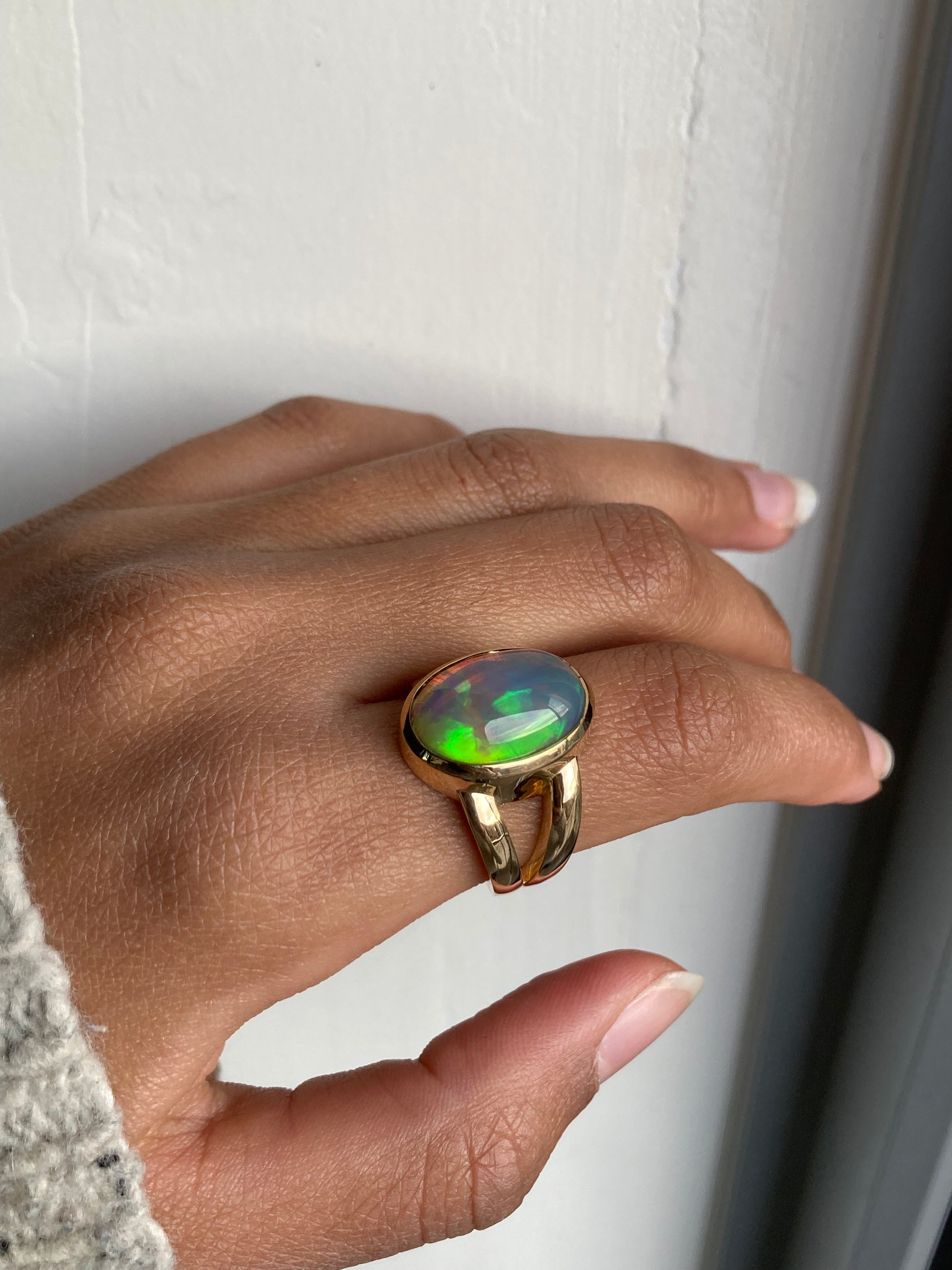 Large Oval cut Black opal with green fire bezel set in solid 14k yellow gold statement ring with split shank. Worn on model's hand