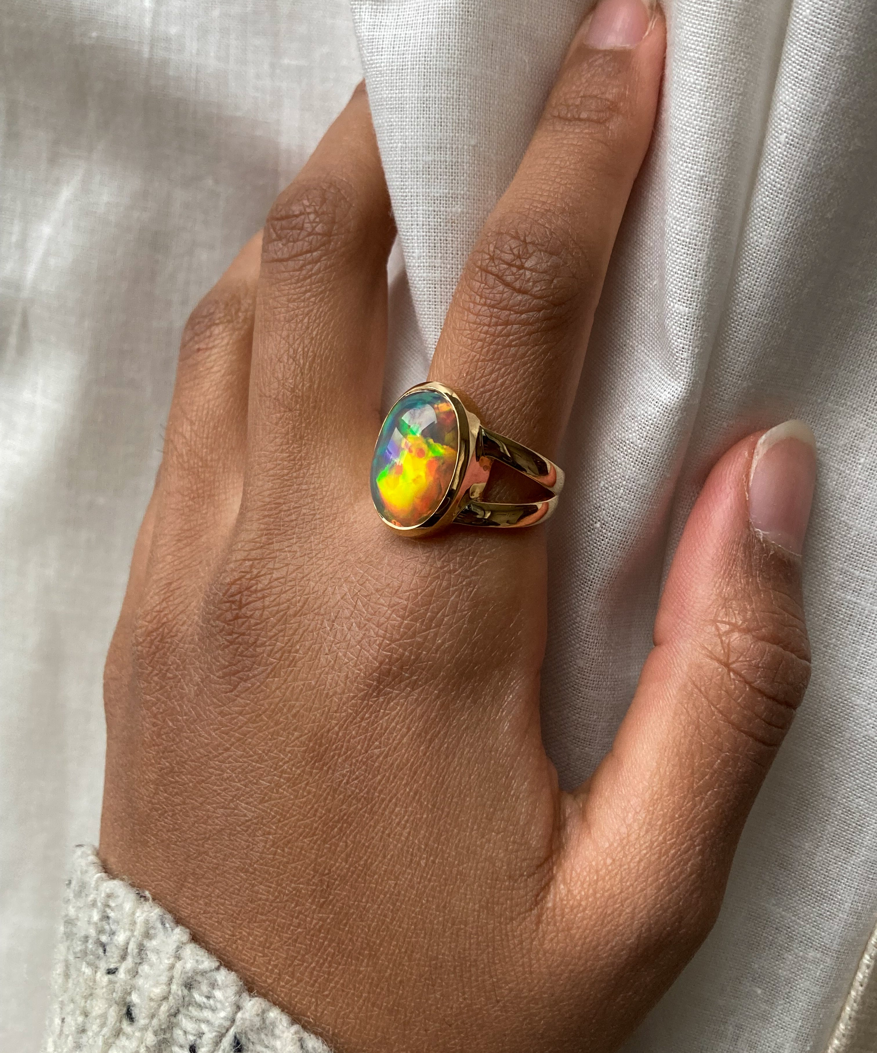 Large Black opal with rainbow and red fire bezel set statement ring with split shank worn on model's hand