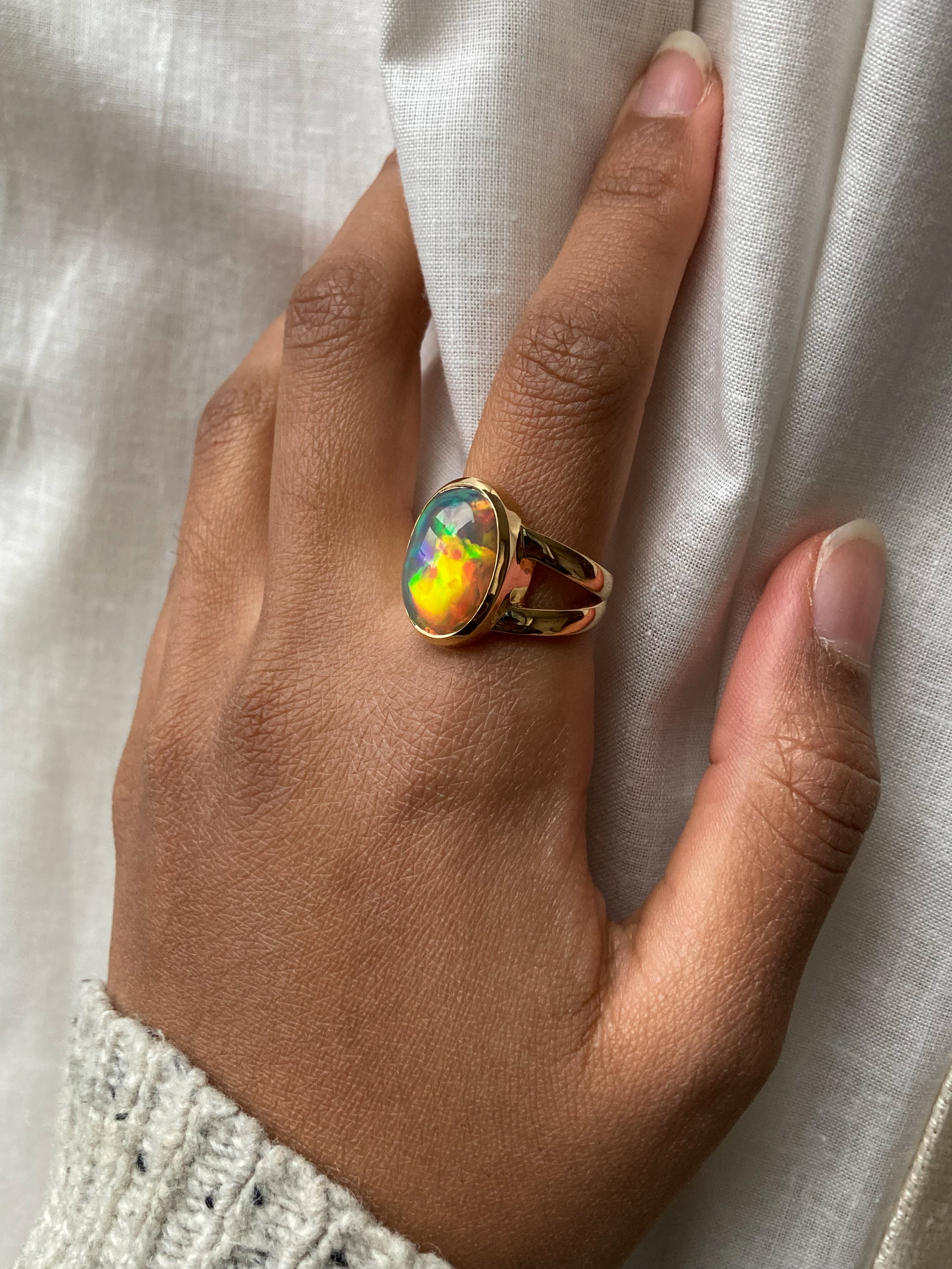 Large Black opal with rainbow and red fire bezel set statement ring with split shank worn on model's hand