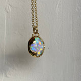 Side view of a solid 14k yellow gold pendant with a white Ethiopian opal with bright rainbow fire held in a bezel setting the shape of a four leaf clover, with a gold chain.