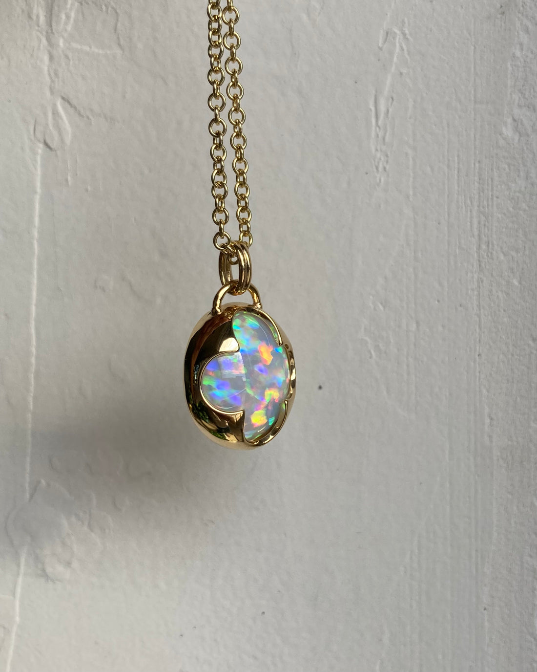 Side view of a solid 14k yellow gold pendant with a white Ethiopian opal with bright rainbow fire held in a bezel setting the shape of a four leaf clover, with a gold chain.