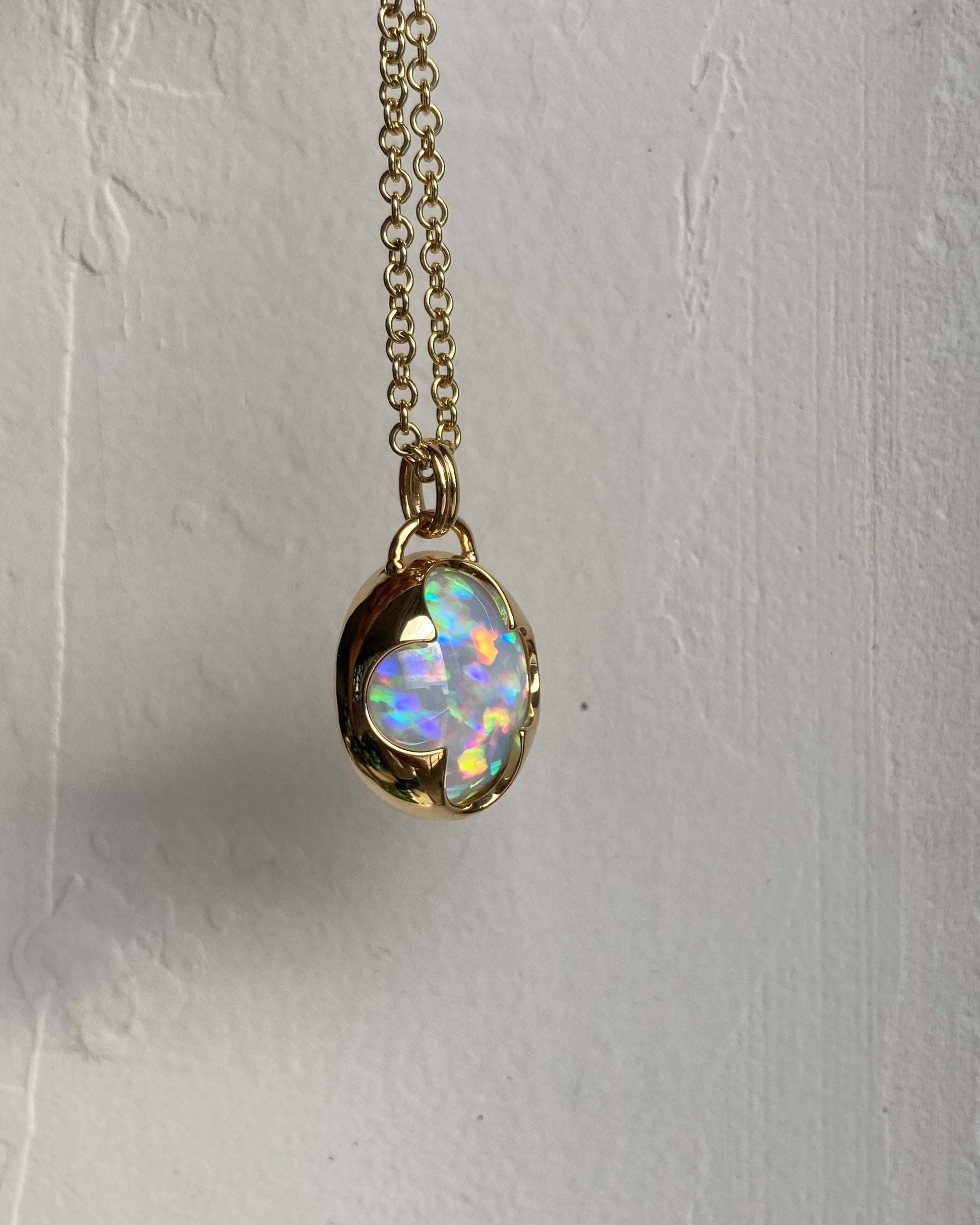 Side view of a solid 14k yellow gold pendant with a white Ethiopian opal with bright rainbow fire held in a bezel setting the shape of a four leaf clover, with a gold chain.