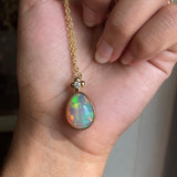 Opal and diamond yellow gold pendant on a gold chain held in a hand