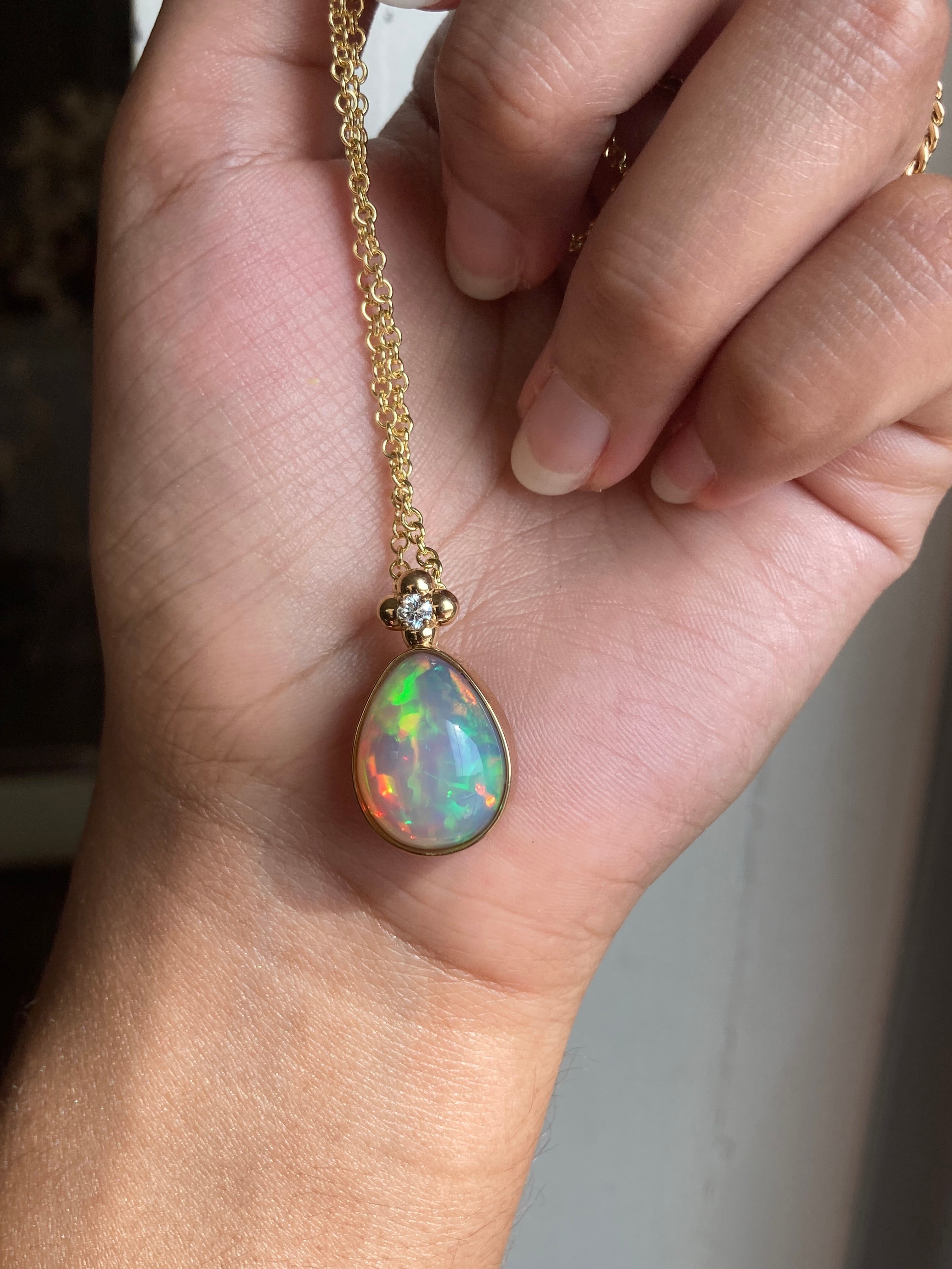 Opal and diamond yellow gold pendant on a gold chain held in a hand