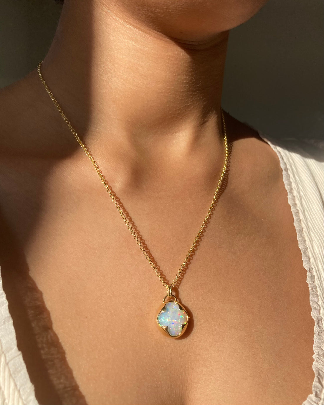 a solid 14k yellow gold necklace with a white opal gemstone with rainbow fire held in a bezel setting the shape of a four leaf clover, with a gold chain.