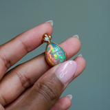 14k solid yellow gold Ethiopian Opal pendant with diamond accent and gold granulation beading flower. Held between fingers against a neutral background.