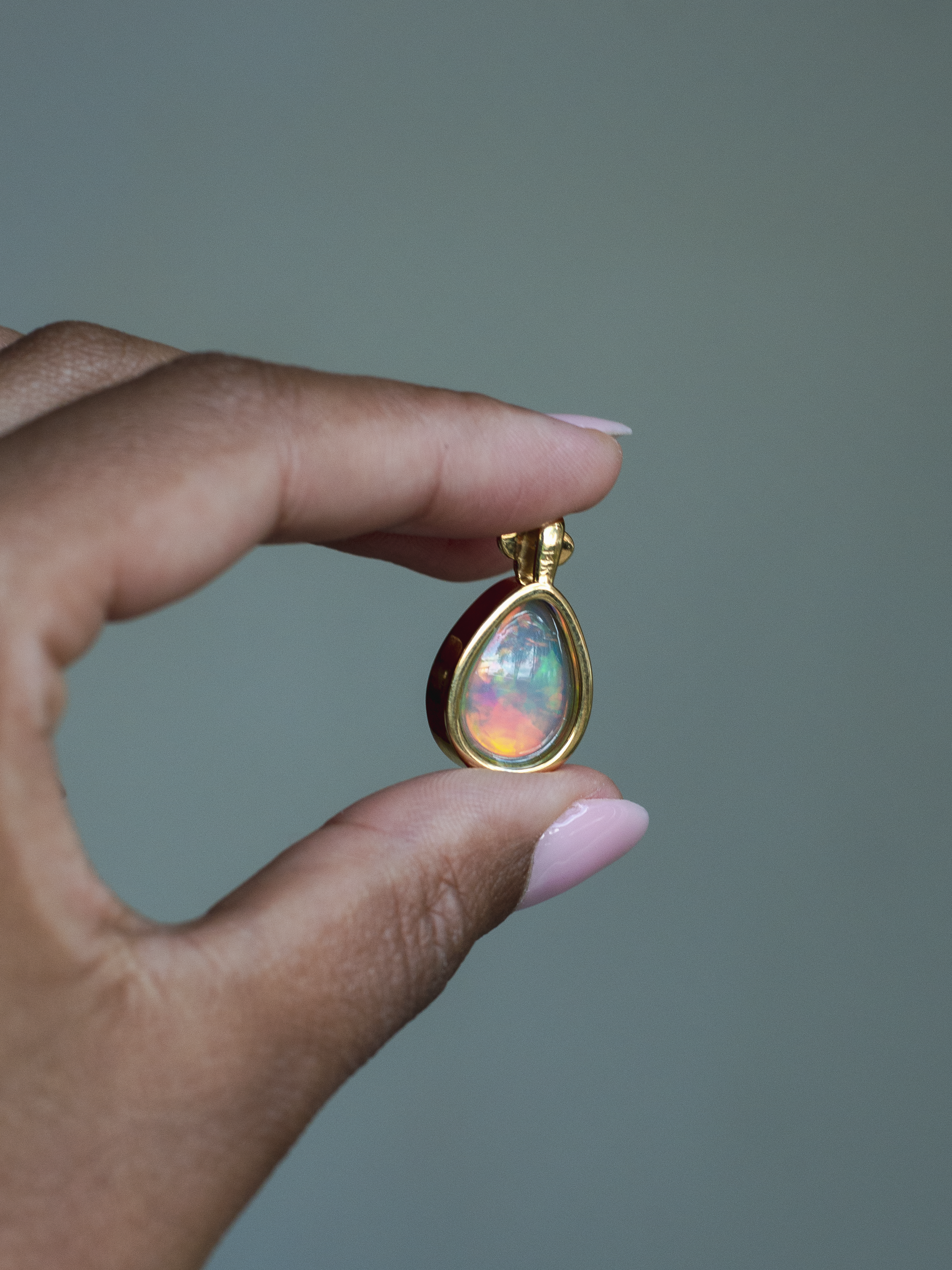 Back side of 14k solid yellow gold Ethiopian Opal pendant with diamond accent and gold granulation beading flower. Held between fingers against a neutral background.