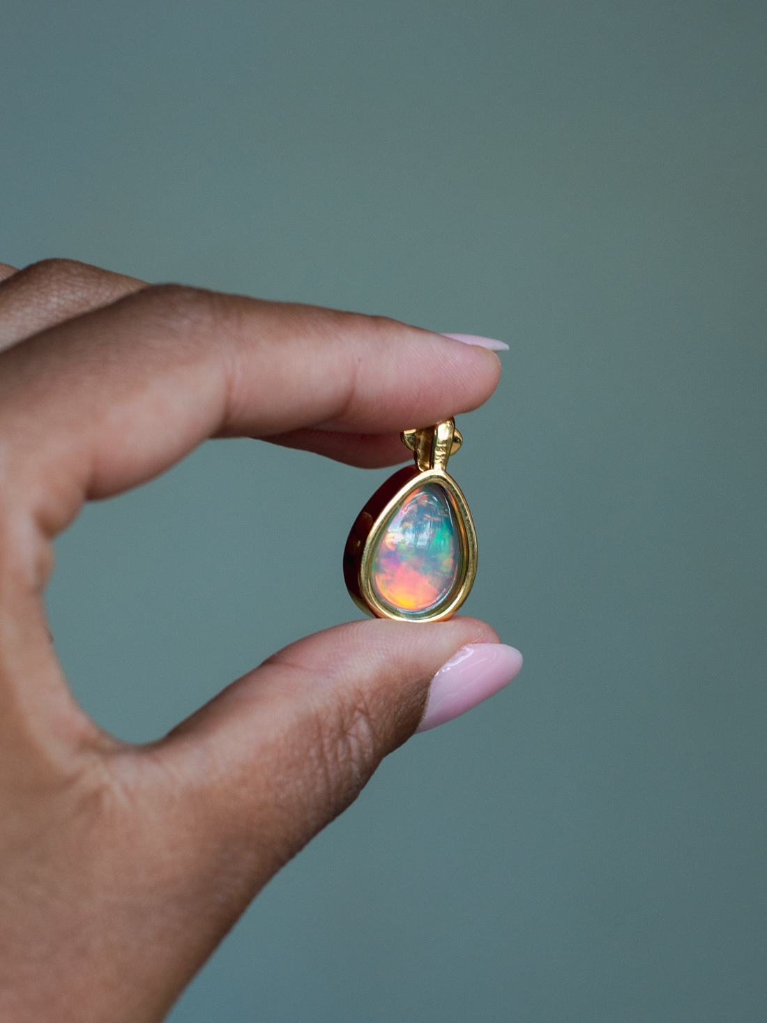 Back side of 14k solid yellow gold Ethiopian Opal pendant with diamond accent and gold granulation beading flower. Held between fingers against a neutral background.