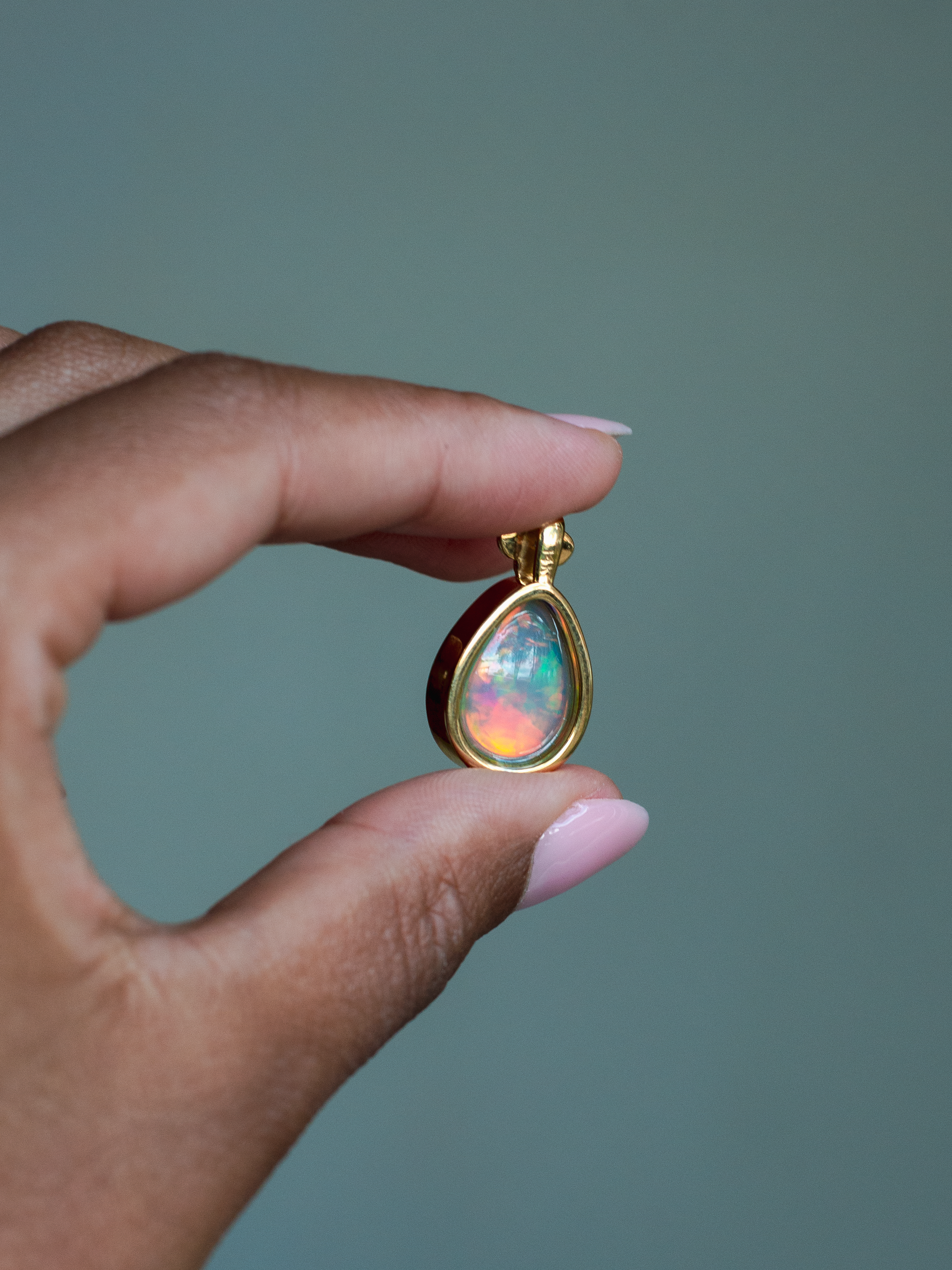 Back side of 14k solid yellow gold Ethiopian Opal pendant with diamond accent and gold granulation beading flower. Held between fingers against a neutral background.