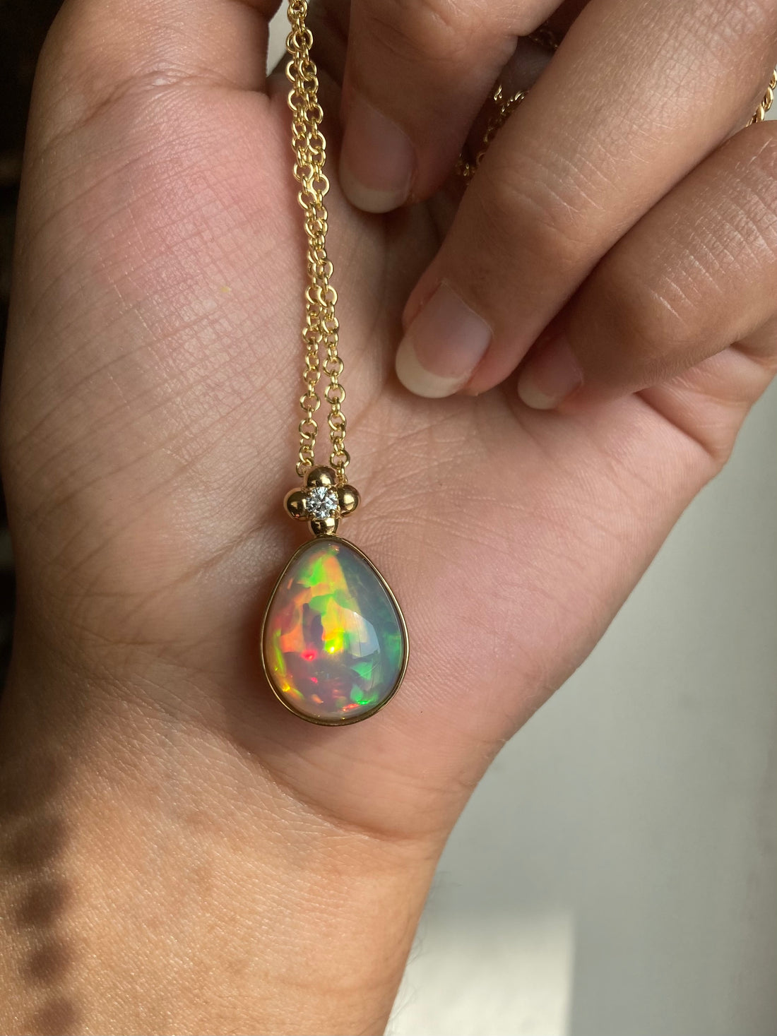 Solid gold Ethiopian Opal pendant necklace held in a hand