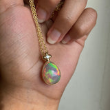 Hand holding a gold necklace with a high quality opal pendant.