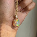 Gold necklace with a teardrop-shaped opal pendant held by a hand.