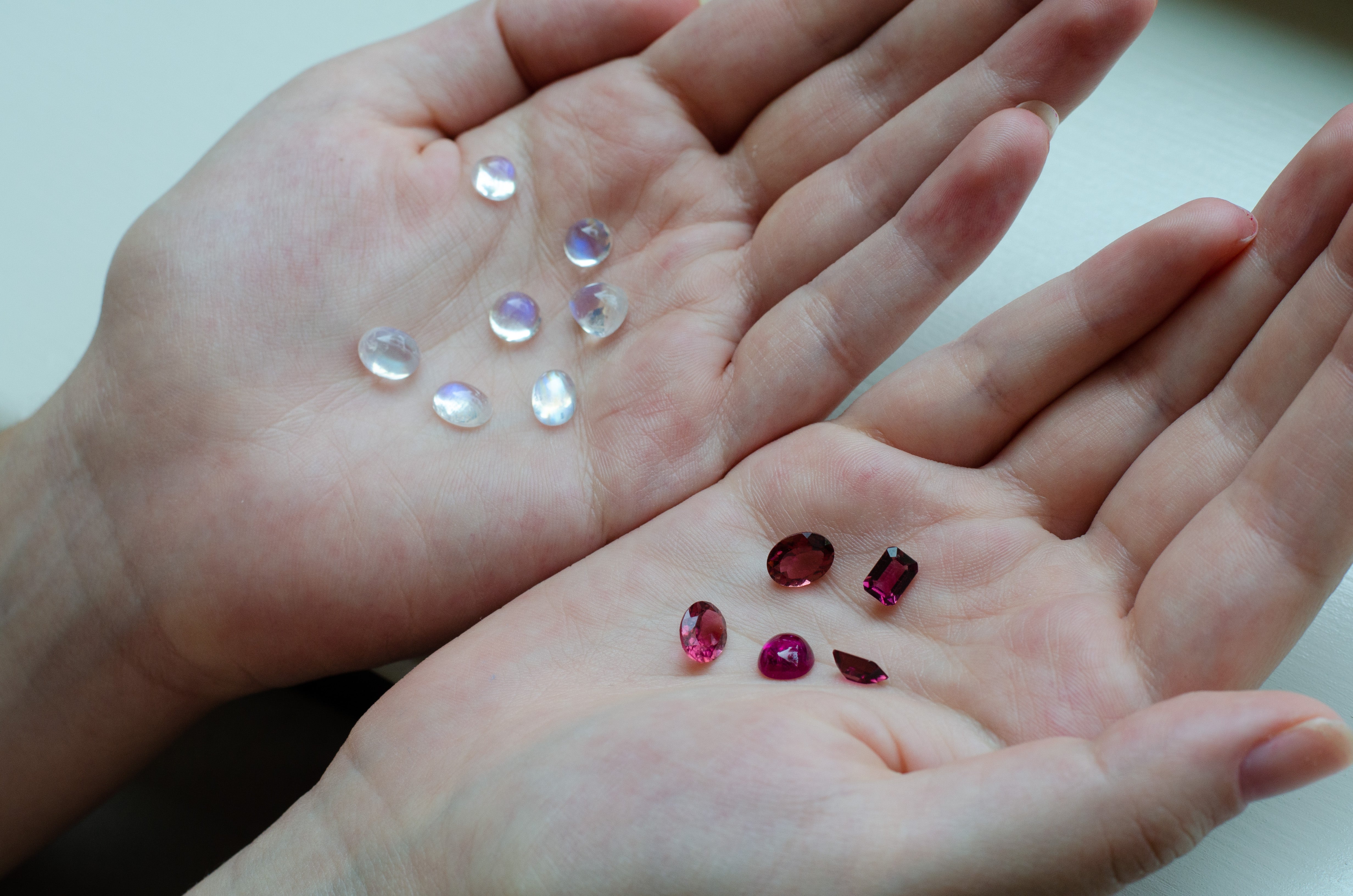 hands holding loose moonstone and pink rubellite tourmaline gemstones