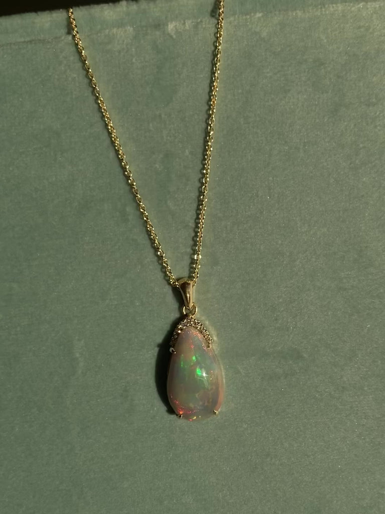 14k solid yellow gold black opal  teardrop necklace with diamond accents sparkling in the sunlight. against a sage green velvet background